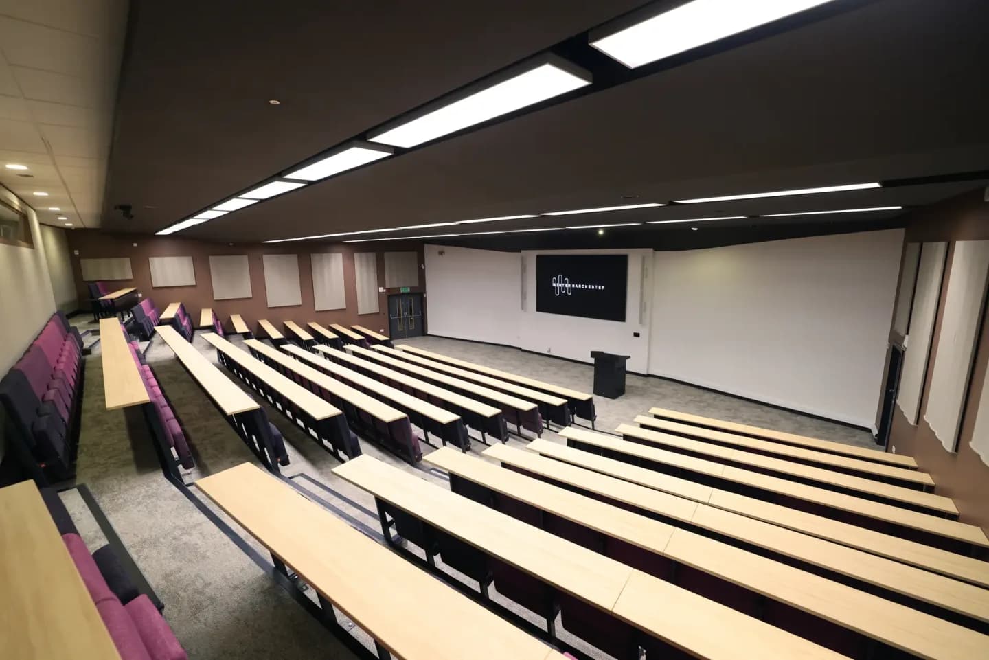 Large lecture theatre at Sister with bench seating and a presentation screen